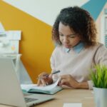 Freelancer writing in a notebook while planning monthly expenses